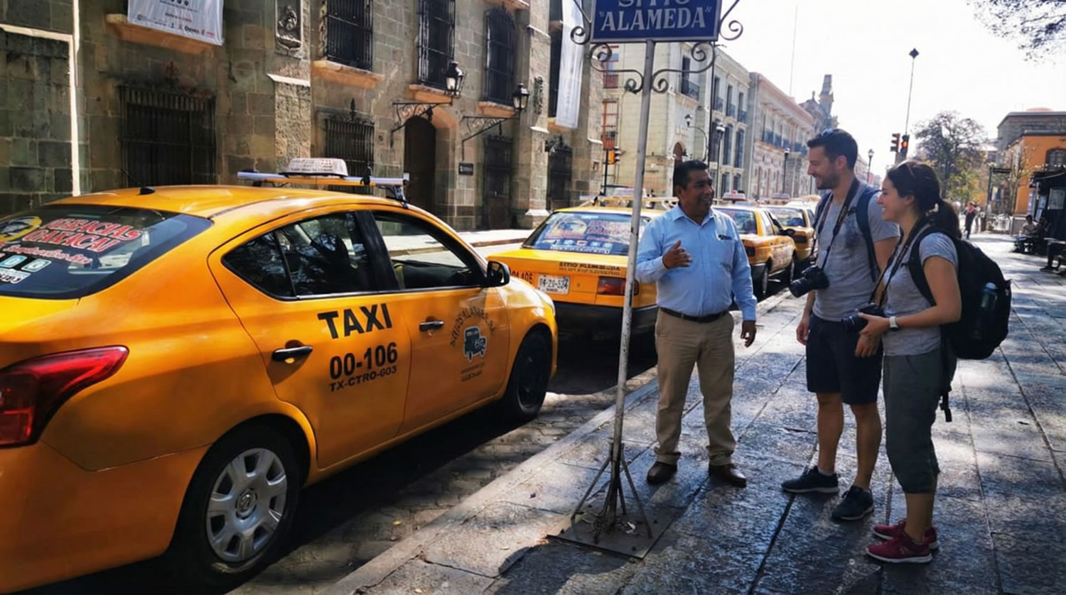 Taxis coloridos formados en una calle concurrida del centro de Oaxaca, con edificios coloniales al fondo.